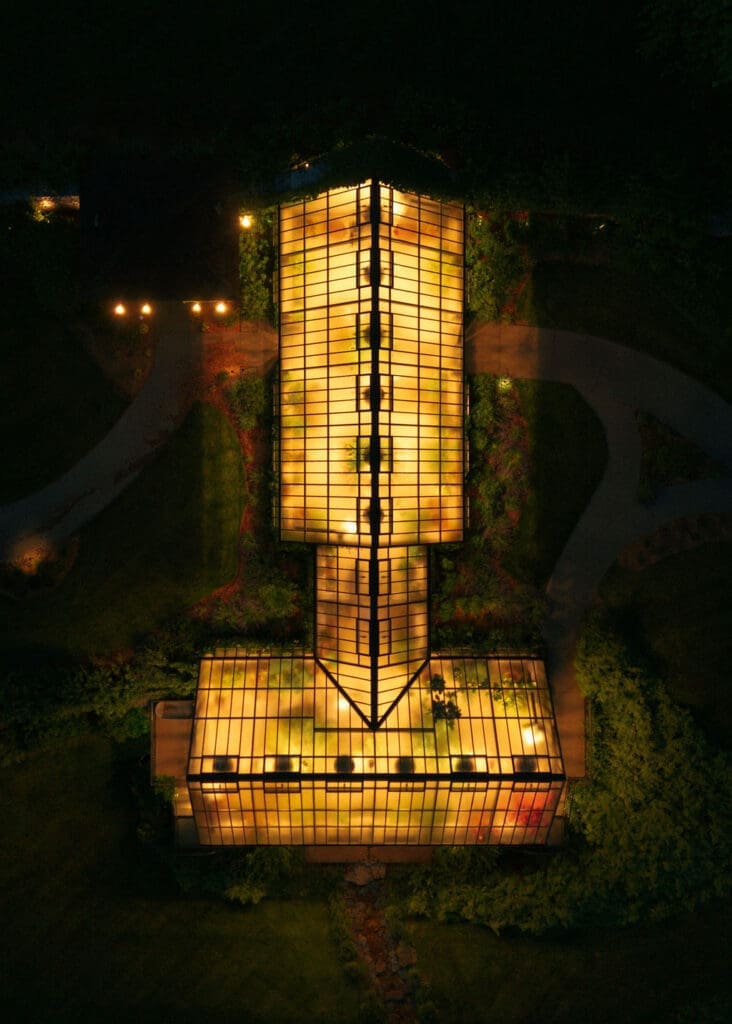 A night drone shot of a greenhouse all lit up. 