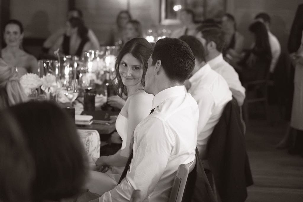A black and white image of the bride and groom looking at each other during speeches. 